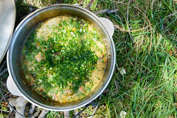 Delicious porridge cous cous with meat, vegetables and fresh herbs in a pot cooking on the nature....
