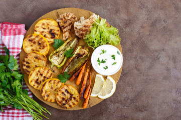 Grilled vegetables, fresh herbs, sauce on a wooden tray. Healthy food. A delicious appetizer. Top view.