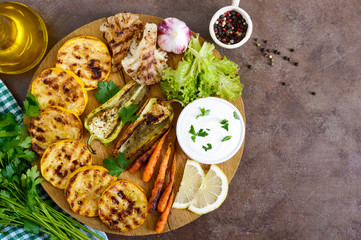 Grilled vegetables, fresh herbs, sauce on a wooden tray. Healthy food. A delicious appetizer. Top view.
