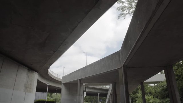 Moving shot of urban overpass on sunny day, lampposts and green trees on the side. Shadows.