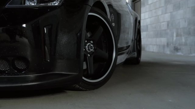 Moving shot of black Nissan sports car focus on the front wheel in a grungy warehouse.