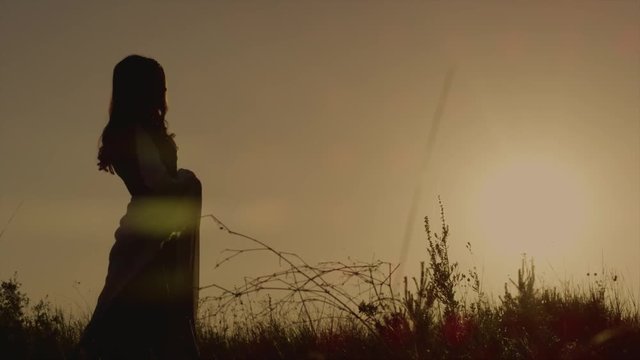 Silhouette of elvish queen walking on the meadow and thinking during beautiful sunset. Lovely woman peacefuly walking alone in forest.
