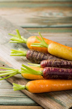 Fresh raw colorful carrots roots, purple, yellow and orange on old wooden table. Healthy food vegetable background with copy space.
