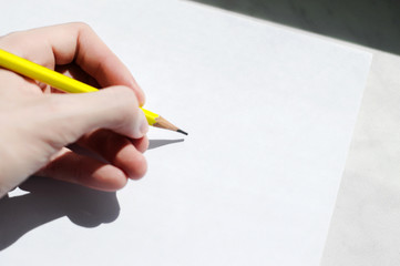 A hand is holding a pencil over a white sheet of paper