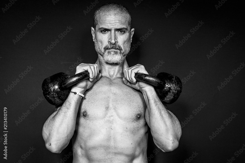 Wall mural A man 50 Y is holding is raising weights. Black background. Black and white.