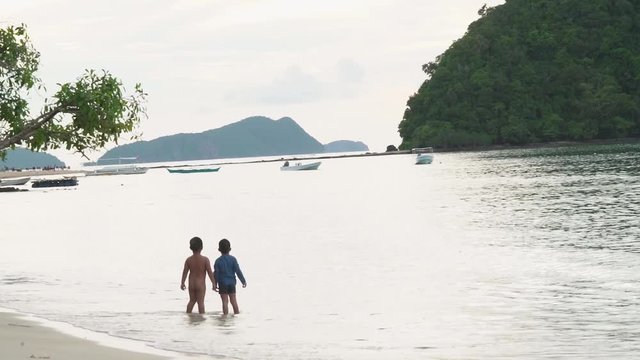 Kids standing at the shoreline of Las Cabanas Beach in El Nido, Palawan Philippines