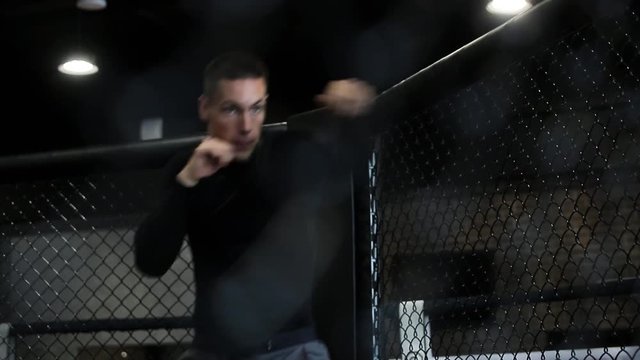 muscular fighter boxing in a black cage at gym.