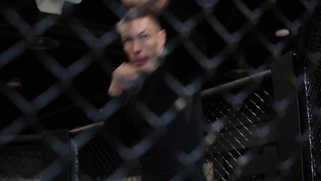 muscular fighter boxing in a black cage at gym.
