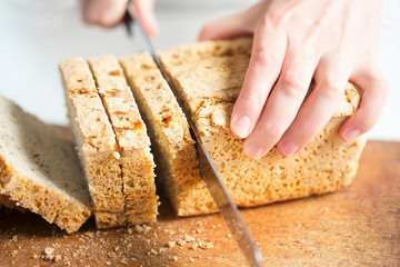 Woman slicing gluten free bread with chickpea, linseed, oat, potato, rye flour