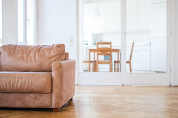 empty couch seat in living room with wooden floor,  and kitchen in background