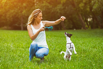 Beautiful woman enjoys playing with her cute dog Jack Russell Terrier in the nature.