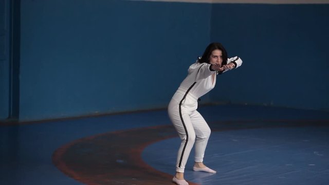 A young girl in a white sports suit performs karate techniques in the sports hall.Comic sport