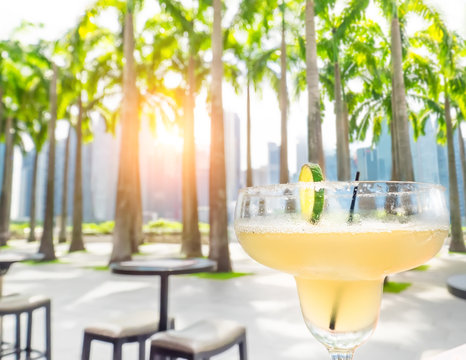 Drinking margarita cocktail in Singapore outdoors cafe. Amazing sunset cityscape  with palm trees and skyscrapers. Luxury vacation in modern asian city