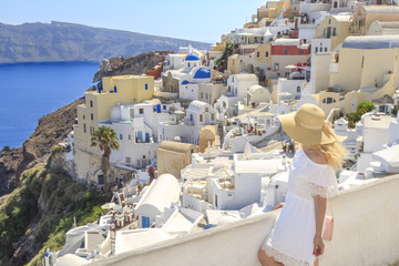 Fototapeta na wymiar Blonde woman looking at cityscape of Oia village in Santorini island, Greece