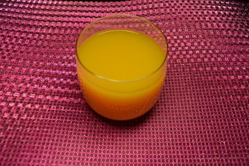 One glass with cold orange juice on a holographic pink background