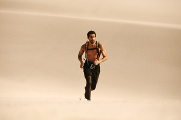 Fototapeta na wymiar Muscular man running on sand dunes