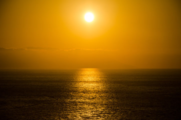 Yellow hazy sunset over a dark, reflective sea