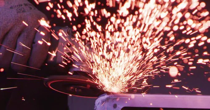 industry worker electric wheel grinding  on steel structure and making sparks in factory small business shop in slow motion