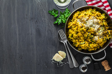 Italian dish yellow Risotto milanese with saffron, zucchini and Parmesan cheese on a black slate table with white wine in a glass. north Italy kitchen. copy space