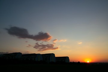 Sunset city landscape, black horizon, golden yellow and red sun, blue sky with colored clouds