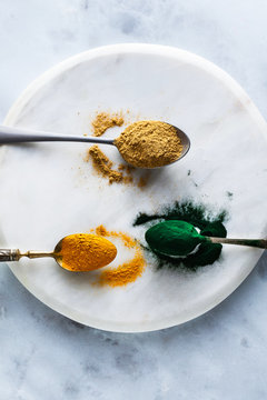 ginger and turmeric powder and hawaiian spirulina in tablespoons on the board and white marble table. healthy supplements, superfoods in cooking