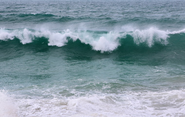 Close up of turquoise waves with white foam crashing before the shore 