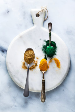 ginger and turmeric powder and hawaiian spirulina in tablespoons on the board and white marble table. healthy supplements, superfoods in cooking
