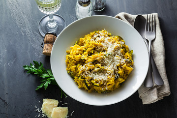 Italian dish yellow Risotto milanese with saffron, zucchini and Parmesan cheese on a black slate table with white wine in a glass. north Italy kitchen