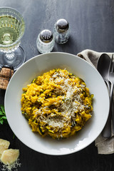 Italian dish yellow Risotto milanese with saffron, zucchini and Parmesan cheese on a black slate table with white wine in a glass. north Italy kitchen