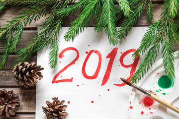 Preparation for design, congratulation merry Christmas, it is written by red watercolor paint. Fir cones and branches were eaten around an inscription. Below a dark wooden background from boards.