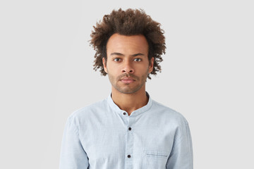 Obraz premium Serious self assured mixed race male with curly hair, looks with concentrated expression, dressed in white shirt, listens attentively recommendations from colleague to improve financial situation