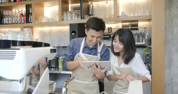 Two young asian barista man and woman using tablet computer during a break on the work in the coffee shop.