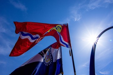 Saint louis city and missouri state flags on poles with arch and sun in background - obrazy, fototapety, plakaty