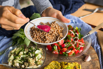 Woman hands spreading tomato dip sauce with sour plums and ajika on Russian traditional buckwheat porridge. Raw vegan vegetarian food. Healthy paleo diet. Trendy dieting
