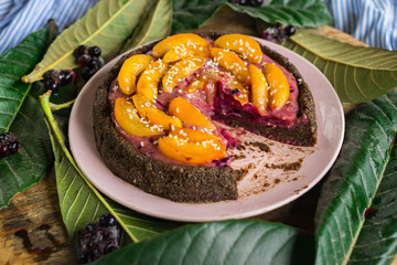 Cut raw vegan pie with apricot and black currant berries cream. Vegan chocolate fruit cake with dates, banana, nuts, cocoa, carob powder. Vegetarian healthy dessert.