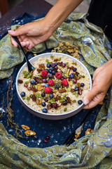 Woman hands holds oatmeal granola porridge with banana, dried fruits, honey and berries. Dates, dried grape, honey, blueberry, raspberry and oats for morning breakfast. Paleo vegetarian diet