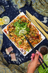 Woman hands holds with chopsticks asian fried noodles with vegetables, prawn and octopus meat cooked in soy sauce. Traditional authentic food in asian cafe or restaurant. Eat with chopsticks