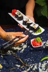 Woman hands holds with chopsticks sushi rolls with tofu, rice, cucumber, avocado, carrot, sour gari - pickled red ginger and wasabi wrapped into nori seaweed. Raw vegan vegetarian healthy food