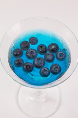 a glass of blueberry in blue water on white background