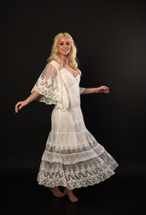Naklejka premium full length portrait of blonde girl wearing white lace dress. standing pose. black studio background.