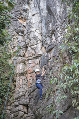 Asian boy in the helmet climbs the rock, kid rock climber sports outdoors.