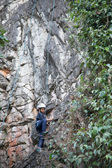 Fototapeta premium Asian boy in the helmet climbs the rock, kid rock climber sports outdoors.