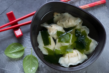 Black bowl of chinese soup with wontons, close-up, view from above on a grey concrete background