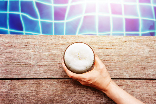 Drinking Beers in Summer r Fall Seson. Hand holding Glass of Beer Lay on the Swimming Poolside. Relaxation on Vacation or Holidays Concept. Top View