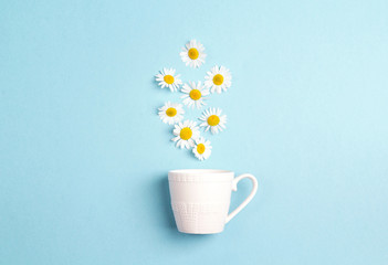 White cup and chamomile flowers on a blue background. Chamomiles come out of the cup like steam.