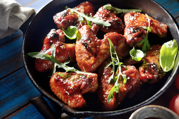Barbecue on the grill chicken wings in a frying pan on a wooden background
