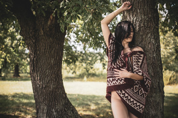 Gypsy girl with long hair posing at nature. A woman with a slim figure and athletic body in knitted sweater, dressed in a sexy kardigan, vintage tones  - obrazy, fototapety, plakaty