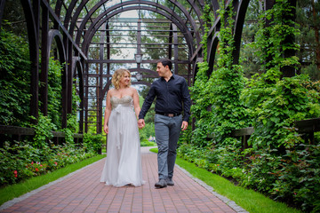 Fototapeta premium Beautiful blonde bride with a magnificent forms in the garden among the flowers in a long light dress. Bride and groom on the walk 