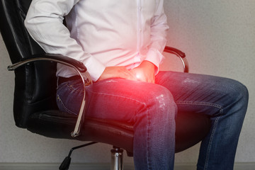 A man sits in an office chair and holds on to the groin, crotch, prostatitis