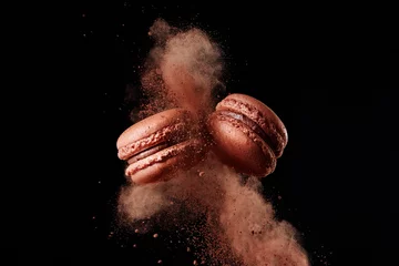  Macaron-explosie. Franse chocolade macaron met cacaopoeder tegen zwarte achtergrond © Melica